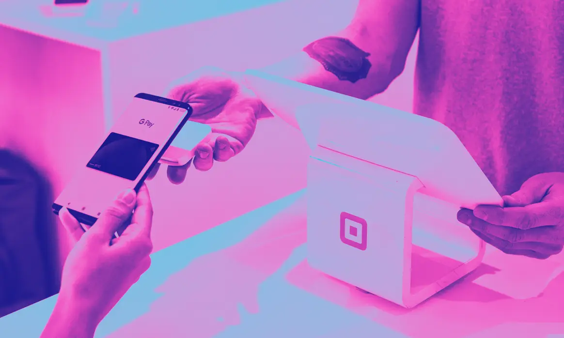 Mãos segurando um celular sobre uma maquineta, em duotom magenta