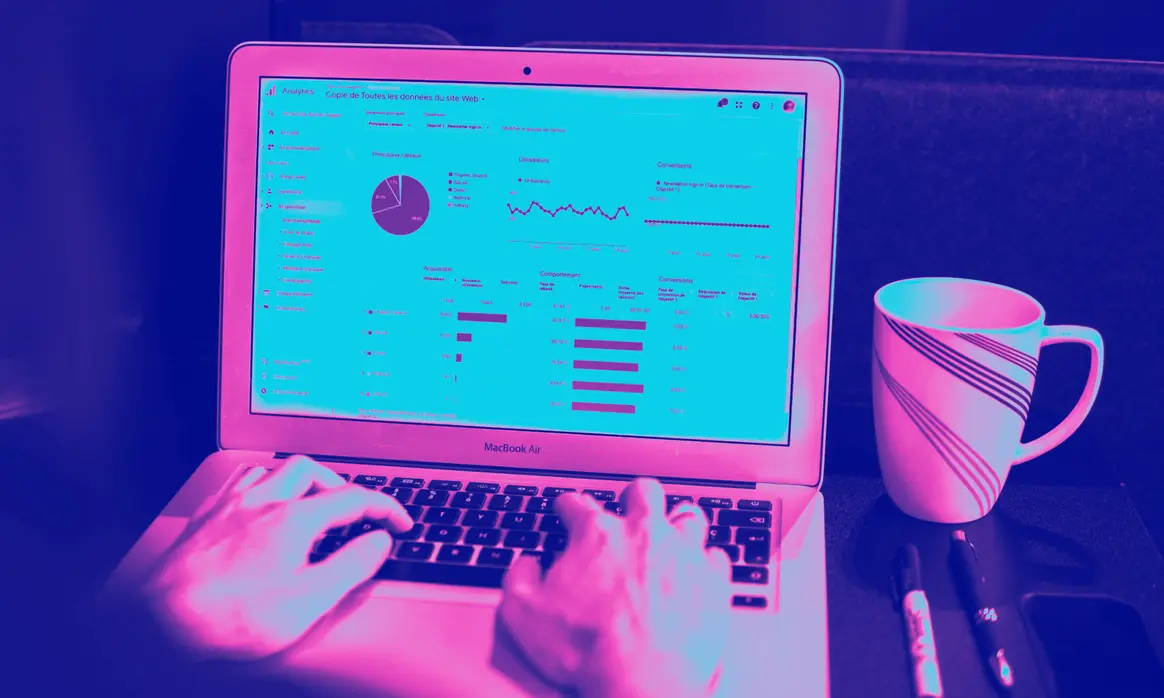 Notebook aberto exibindo um extrato bancário, ao lado de uma caneca, em duotom magenta e azul