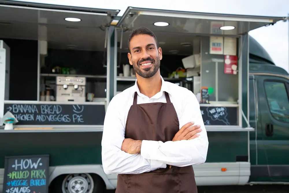 Dono de food truck de braços cruzados na frente do próprio negócio